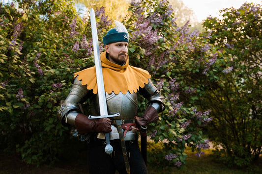 Knight in full medieval armor with teal round cap and longsword by lilac garden