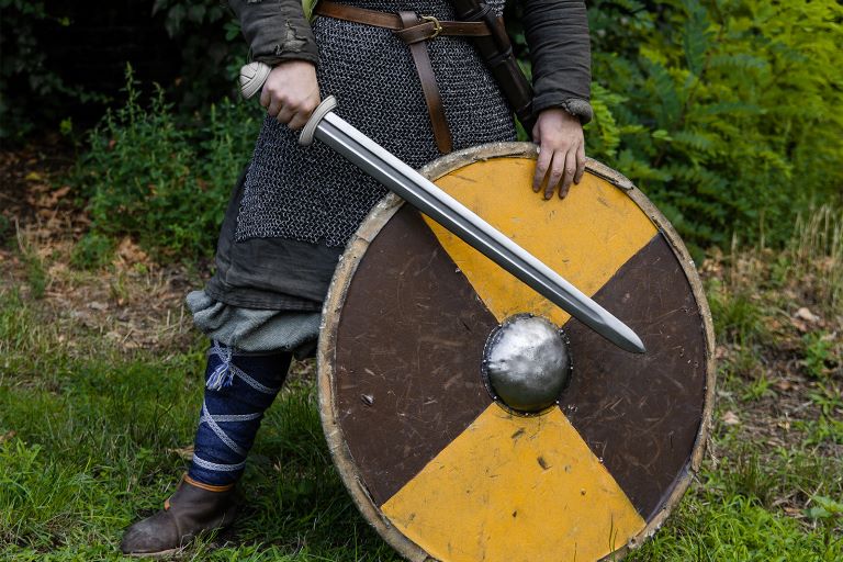 Person in chainmail holding Viking sword Type Z with round shield outdoors