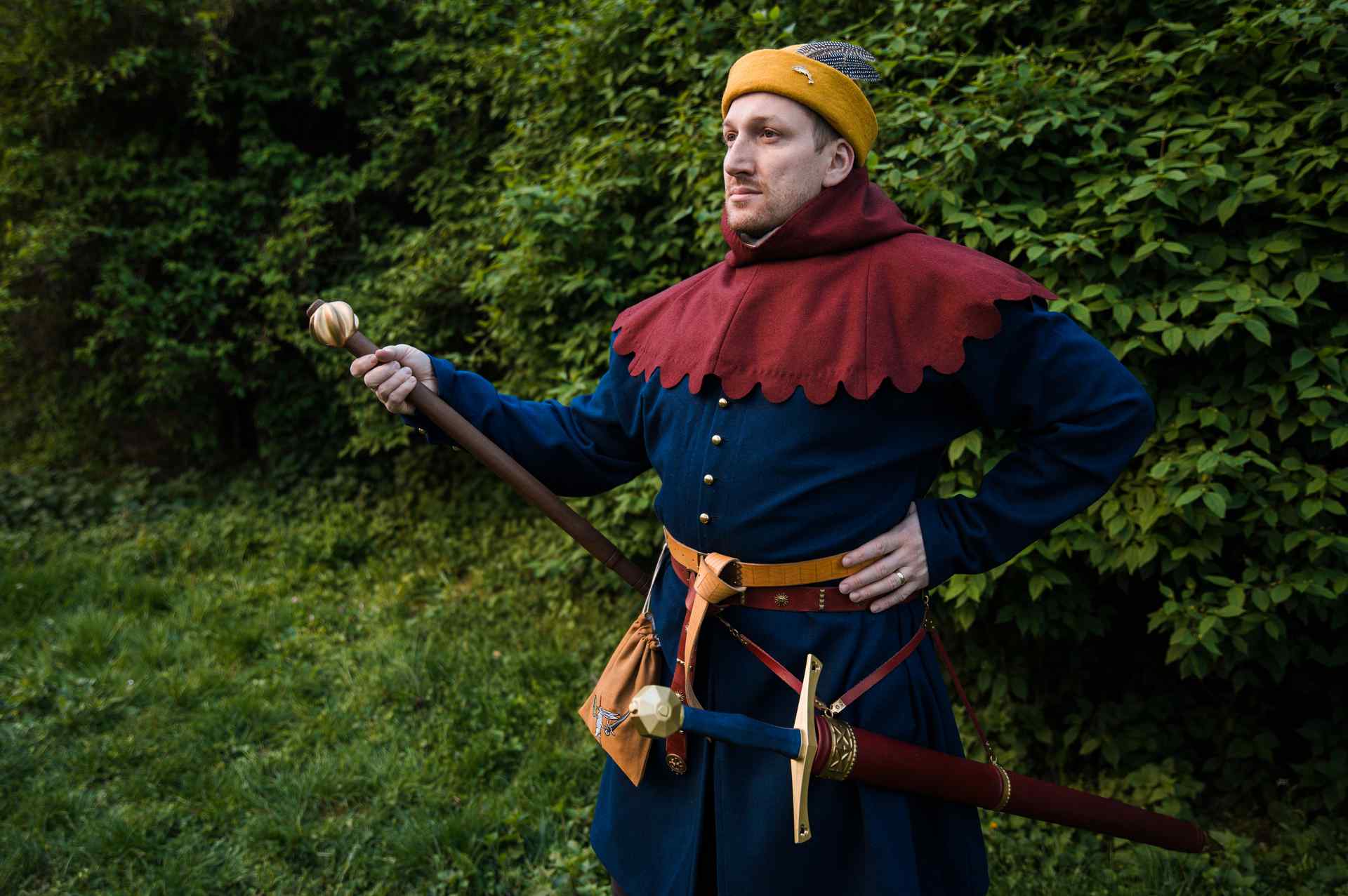 Medieval knight in golden yellow round cap with red collar and sword and mace