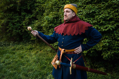 Medieval knight in golden yellow round cap with red collar and sword and mace