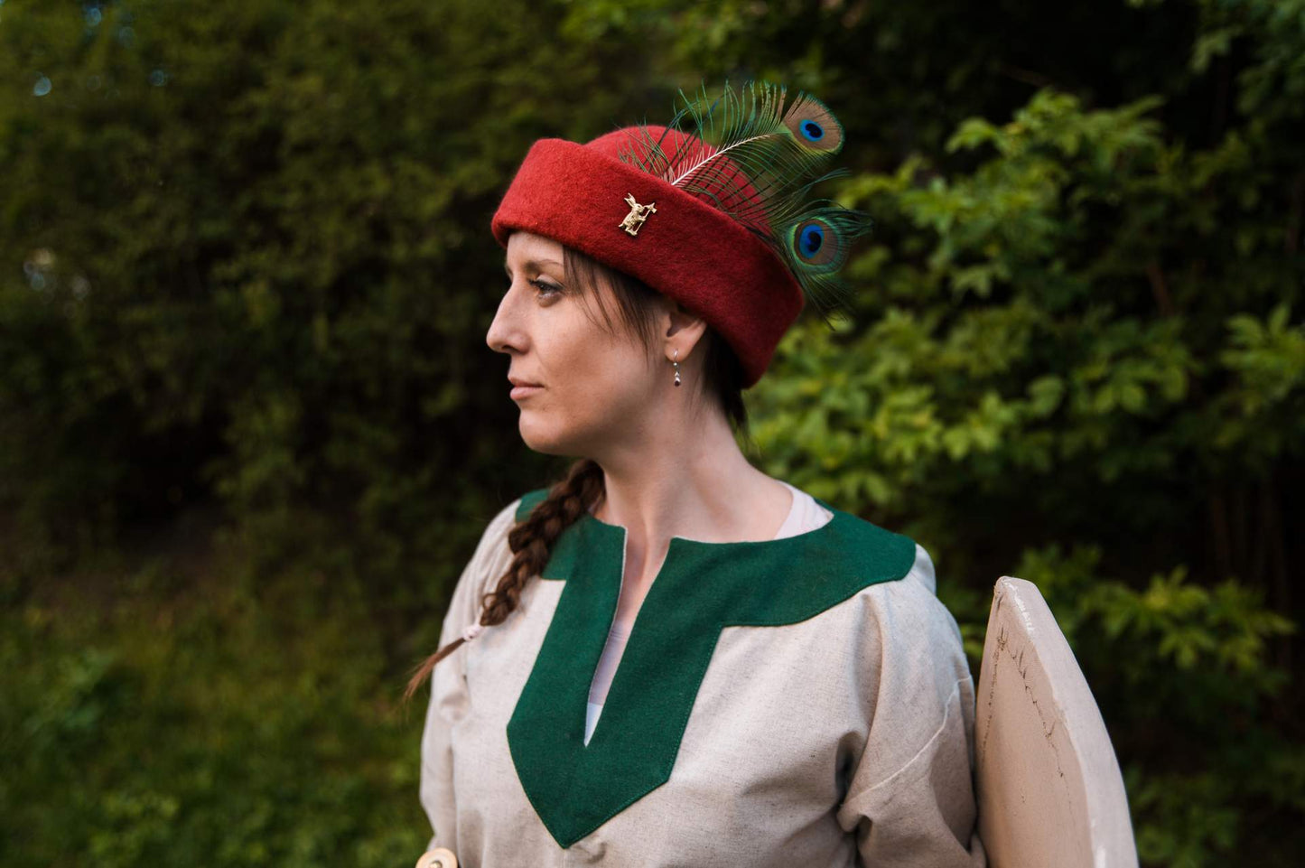 Woman in red wool round cap with peacock feather medieval costume