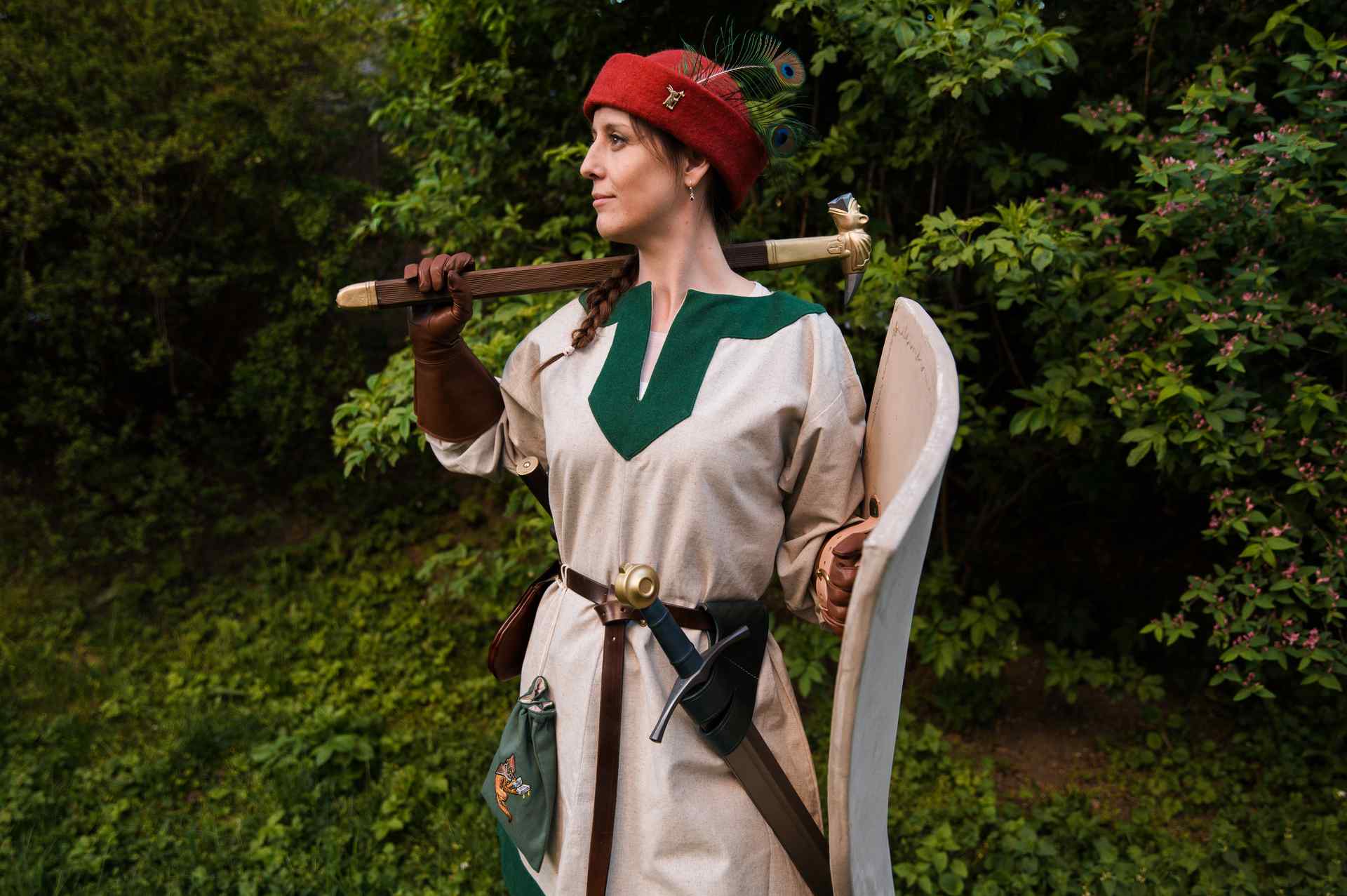 Woman medieval warrior in red round cap with sword and shield medieval costume