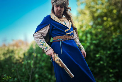 Medieval reenactor in blue coat with fur hat holding wheellock blaster pistol outdoor LARP