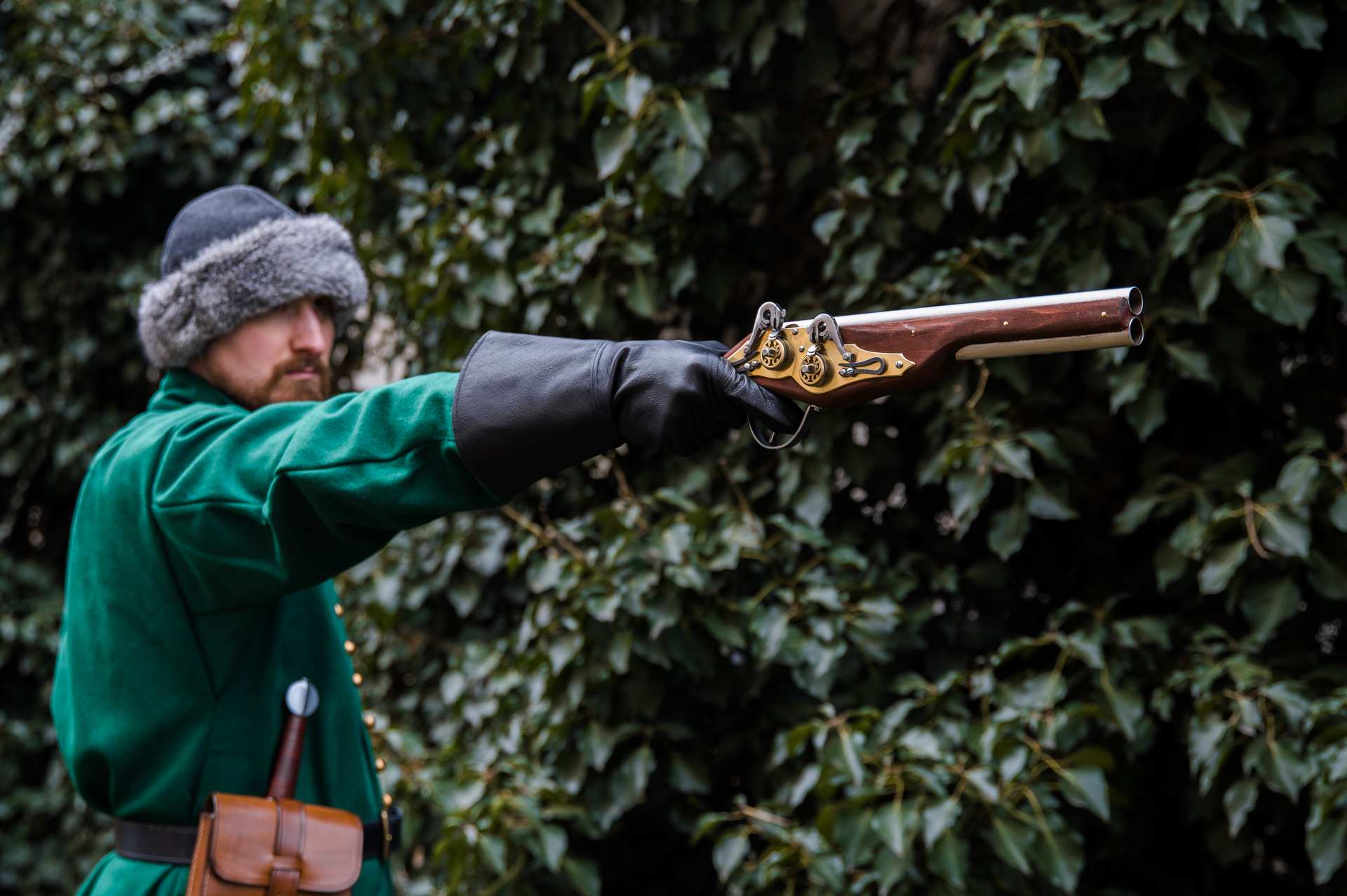 Medieval reenactor in green coat aiming double-barrel wheellock blaster pistol outdoor LARP