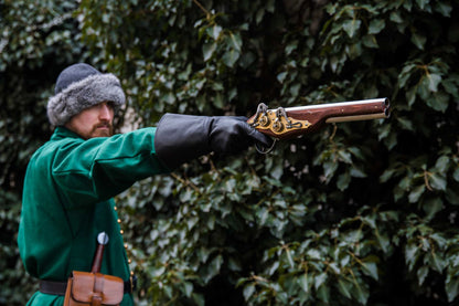 Medieval reenactor in green coat aiming double-barrel wheellock blaster pistol outdoor LARP