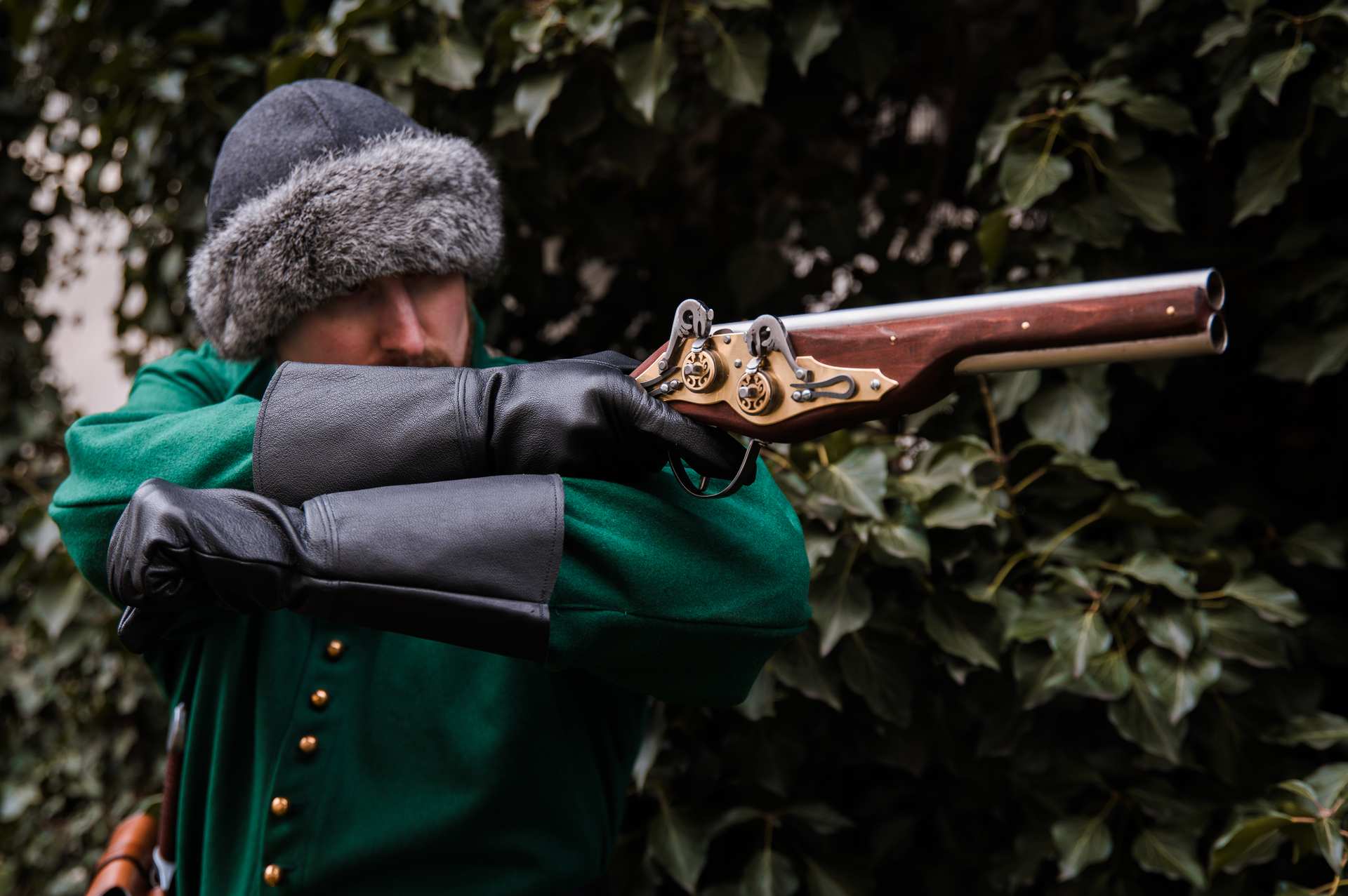 Medieval reenactor in green coat and fur hat aiming double-barrel wheellock pistol LARP weapon