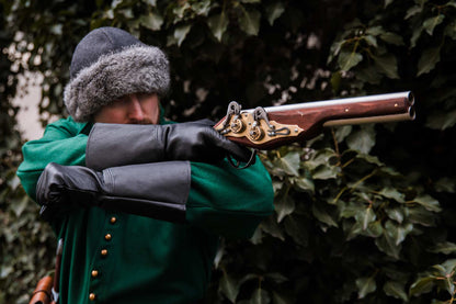 Medieval reenactor in green coat and fur hat aiming double-barrel wheellock pistol LARP weapon