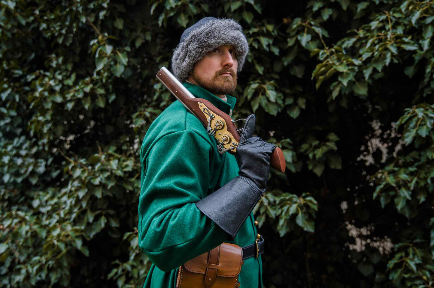 Medieval reenactor in green coat fur hat with wheellock blaster on shoulder outdoor LARP