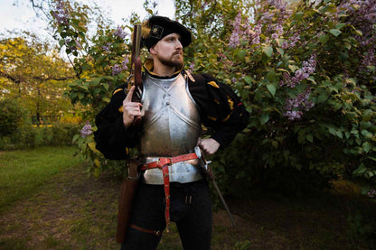 Medieval soldier in armor holding musket in lilac garden with purple flowers LARP weapon