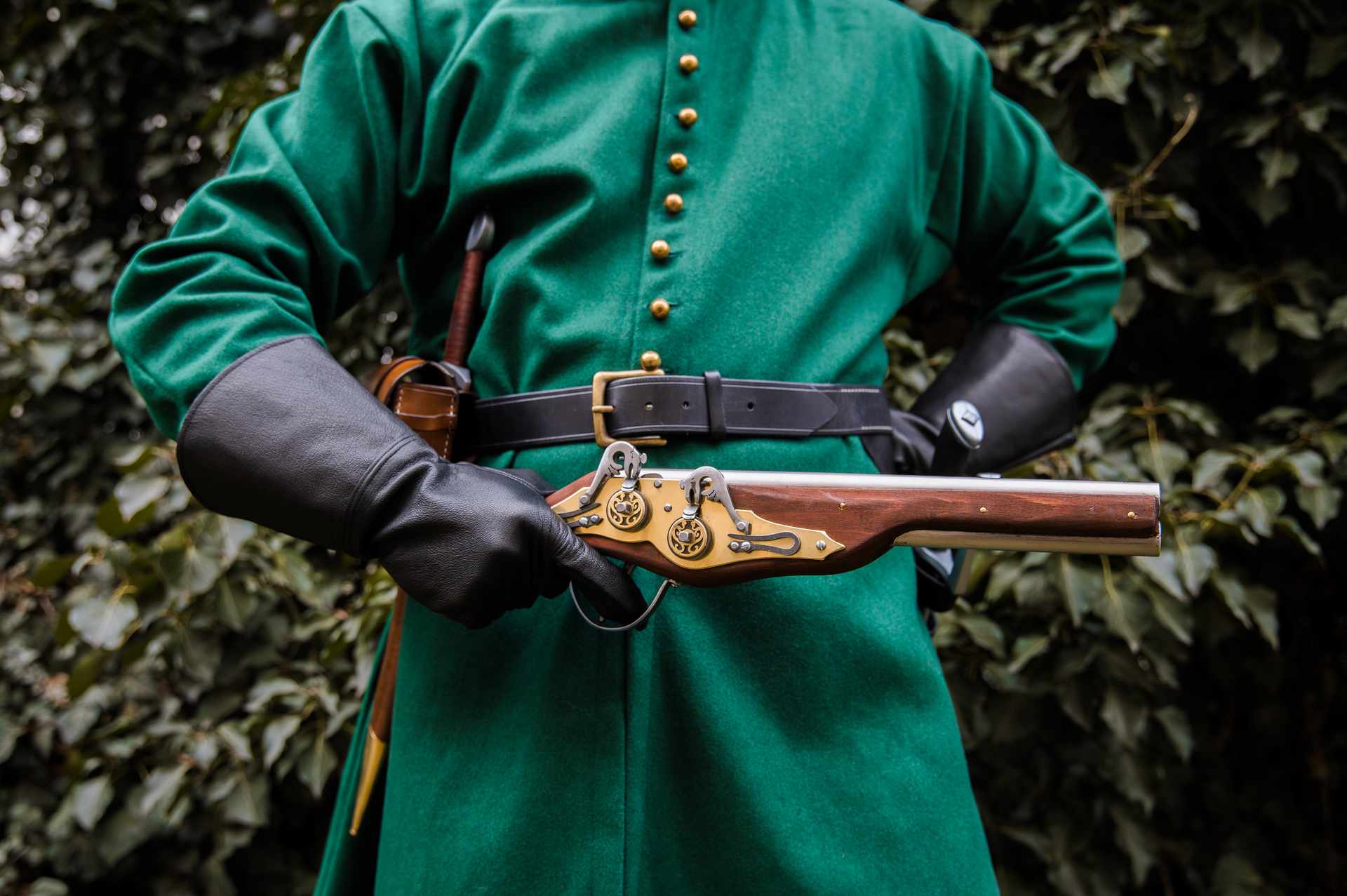 Medieval soldier in green coat with black leather over-under holster holding wheellock blaster closeup