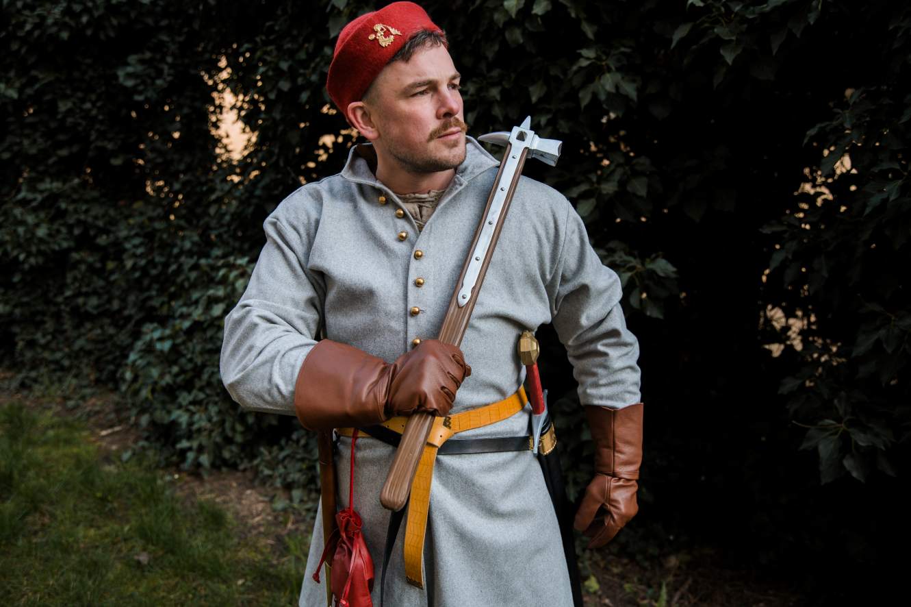 Man in medieval armor and red round cap holding halberd weapon