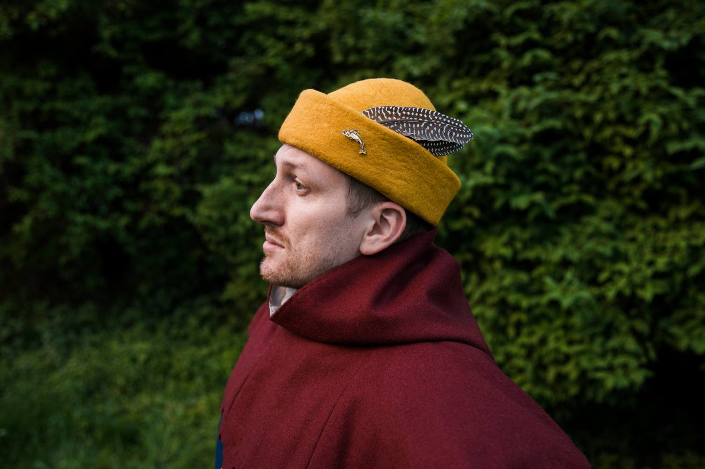 Man wearing yellow wool medieval round cap with guinea fowl feather and brass brooch