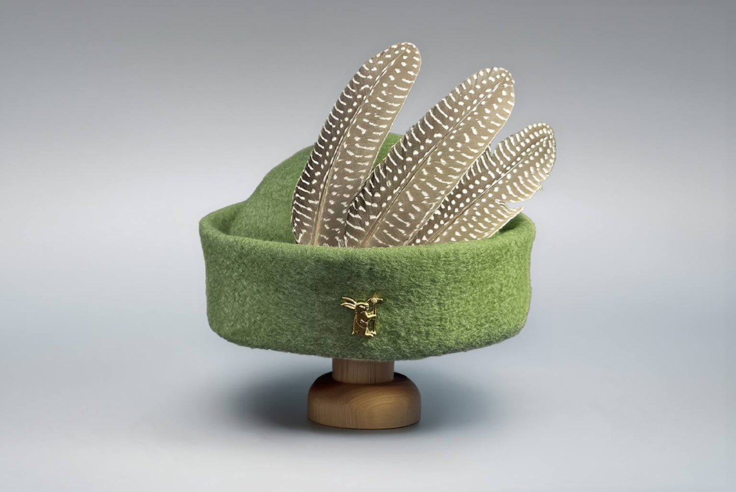 Green round cap wool felt hat with feathers and brass badge on wooden stand display